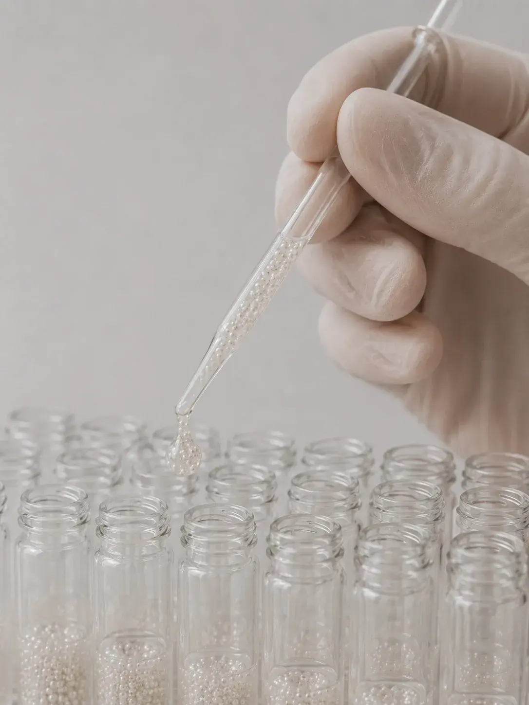 Main gantée en latex tenant une pipette au-dessus d'une rangée de fioles contenant des micro-perles