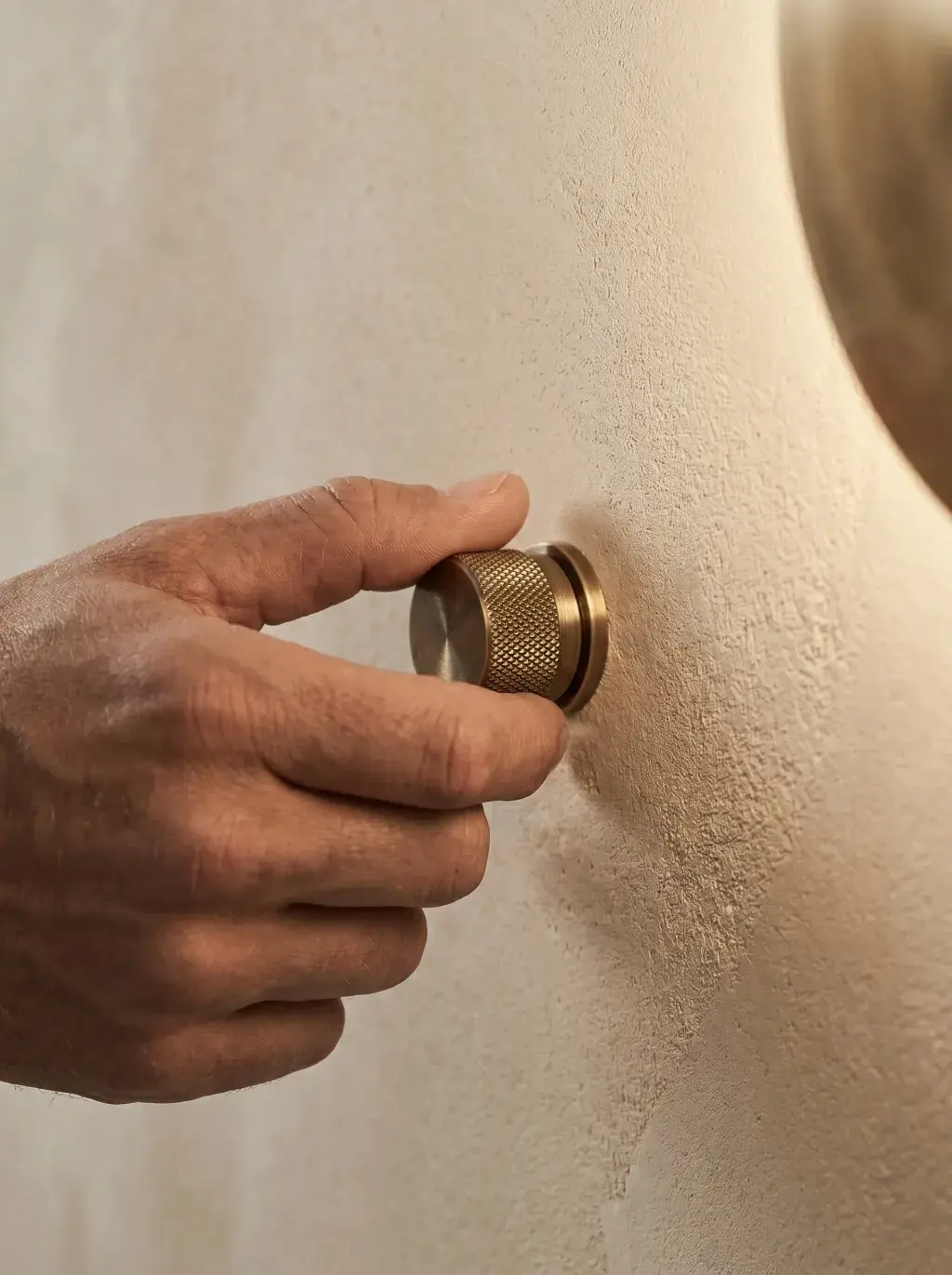 Main posant un variateur rotatif en laiton sur un mur en enduit de terre beige