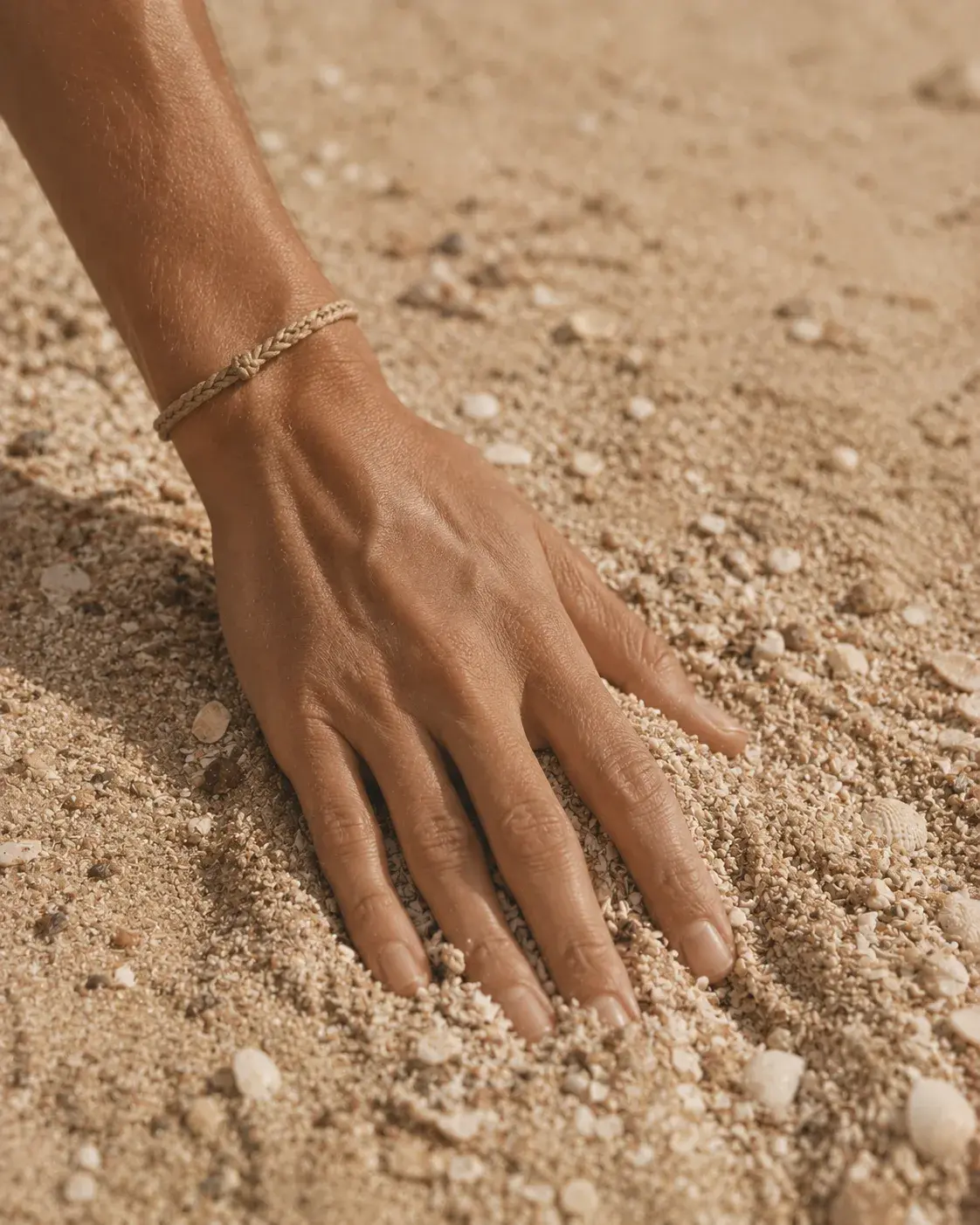 Main posée sur sable fin avec bracelet tressé – gros plan plage sensuelle