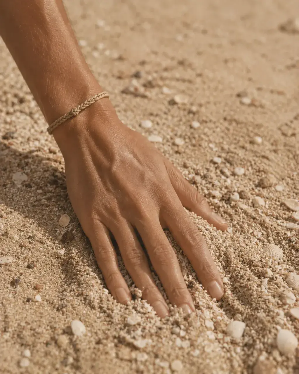 Main posée sur sable fin avec bracelet tressé – gros plan plage sensuelle