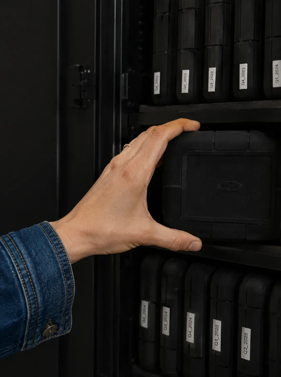 Main saisissant un disque dur externe dans un rack de stockage de disques noirs numérotés et étiquetés