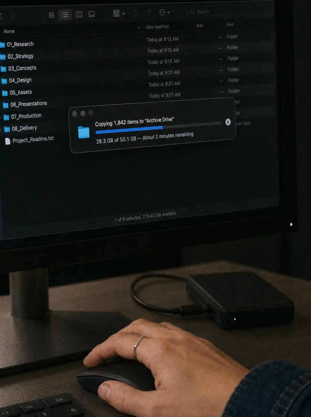 Main sur souris devant macOS sombre affichant la copie de 1 843 fichiers de projet vers disque dur d'archive