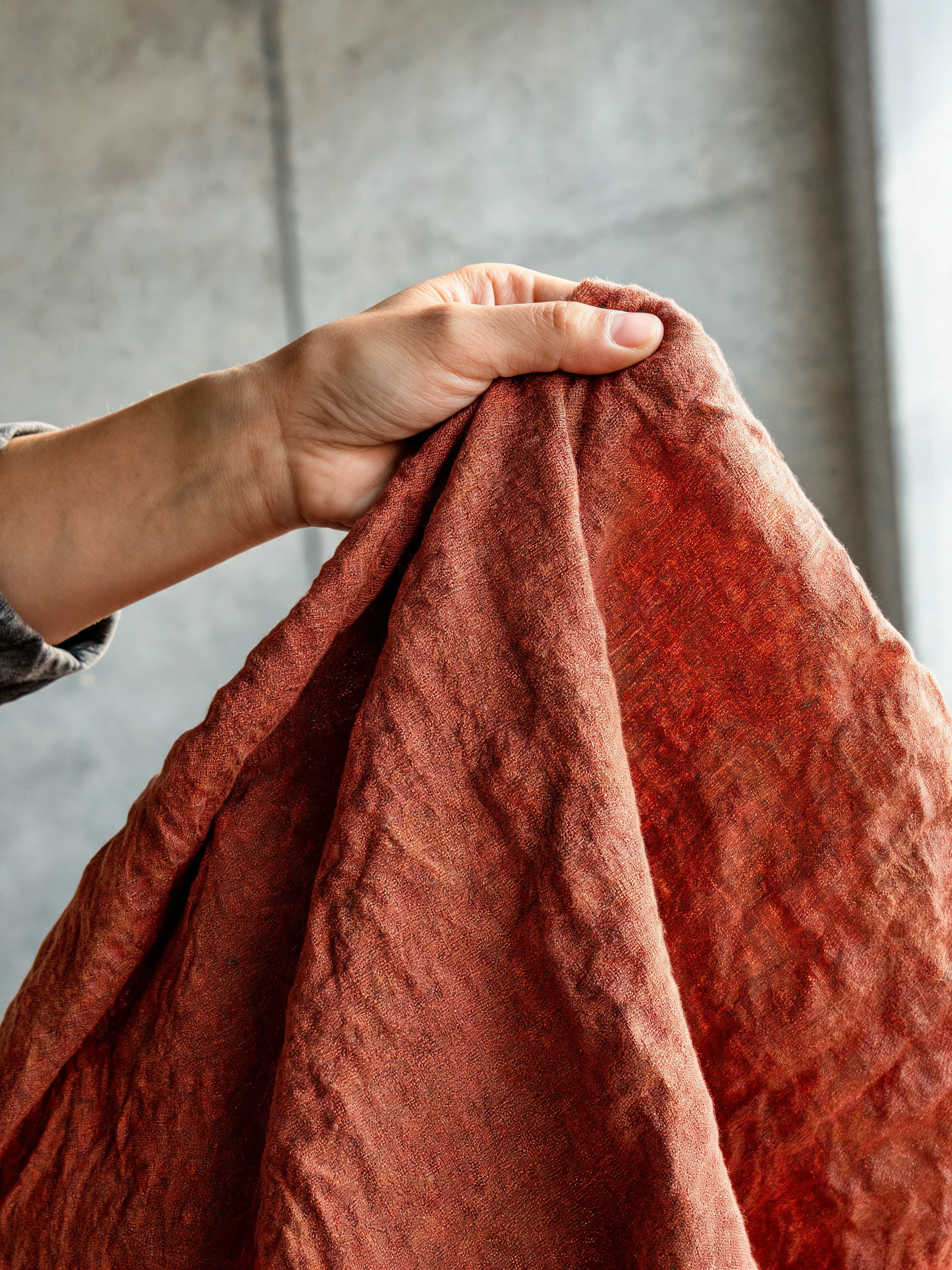 Main tenant tissu lin terracotta froissé – texture naturelle, fond béton gris, studio atelier