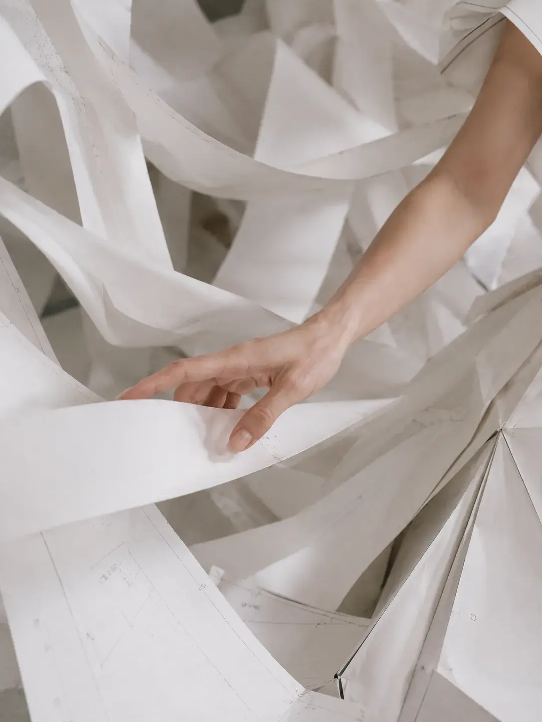Main touchant des rubans de papier froissés – gros plan texture matière blanche