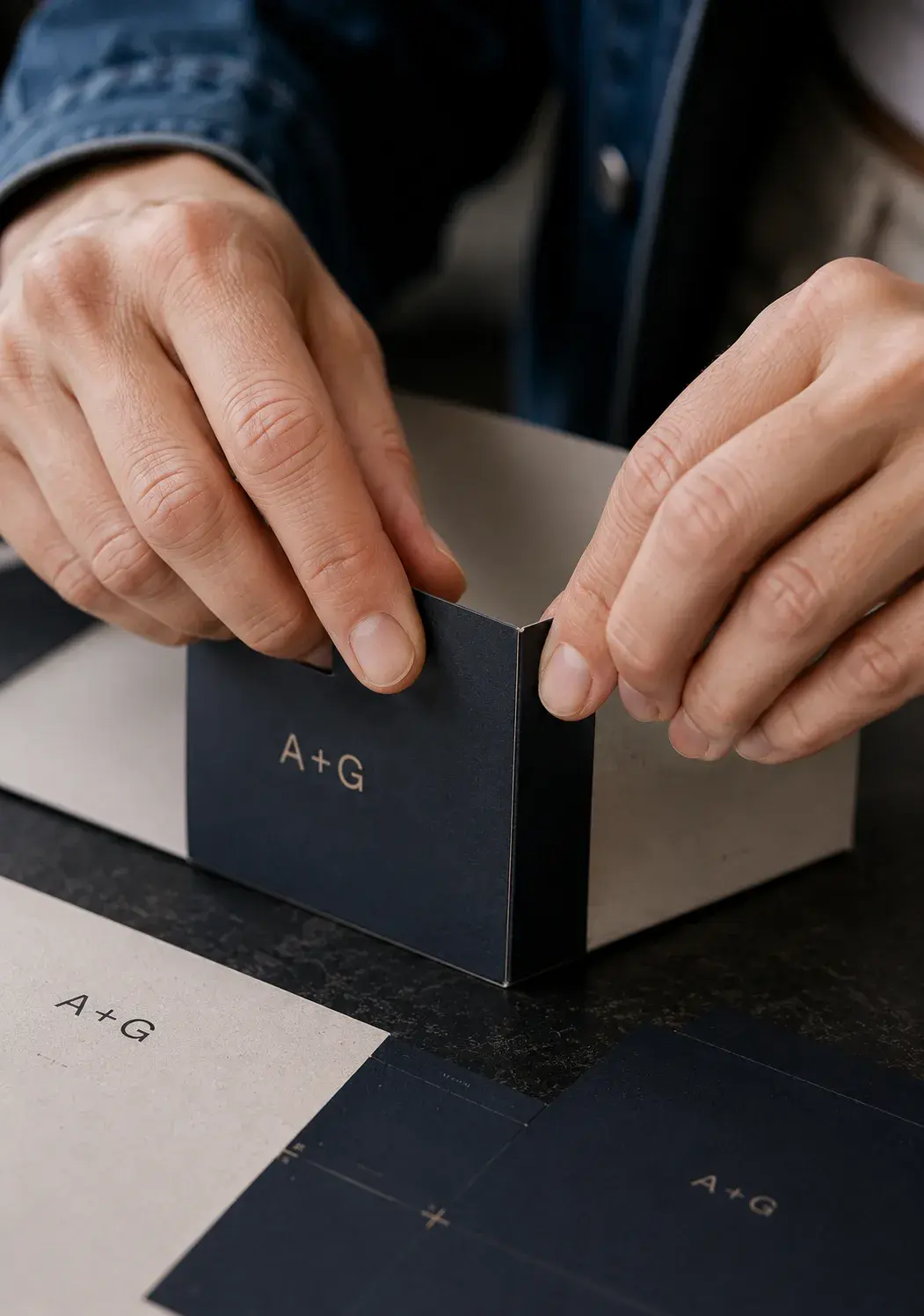 Mains assemblant la boîte de présentation navy A+G Studio avec couvercle sur table de studio