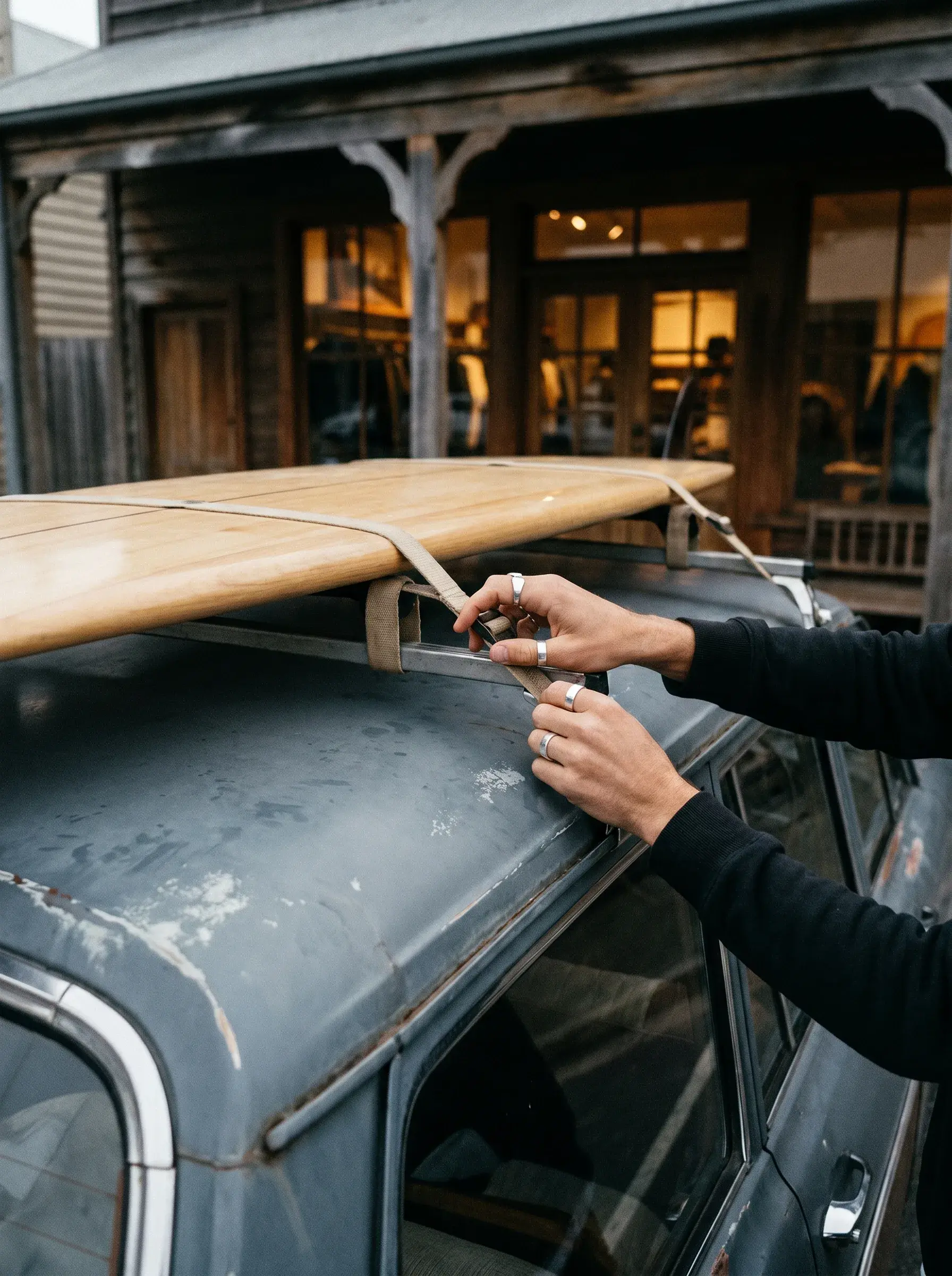 Mains attachant une planche de surf en bois sur le toit d'une voiture vintage avec sangles