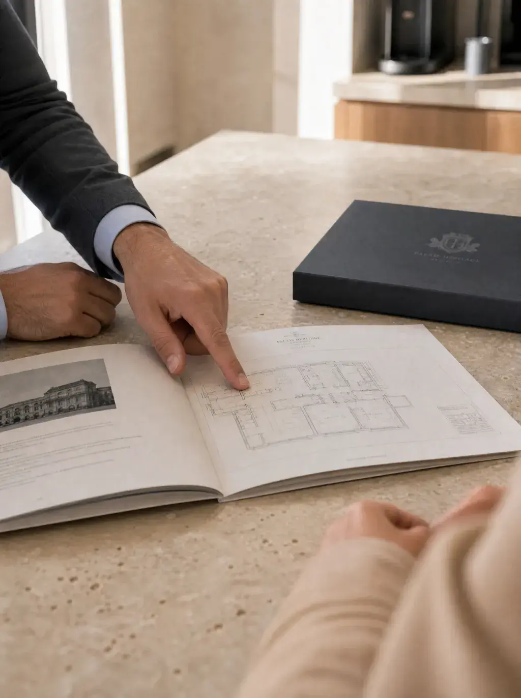 Mains d'agent pointant un plan d'appartement dans une brochure Palais Heritage sur îlot en travertin