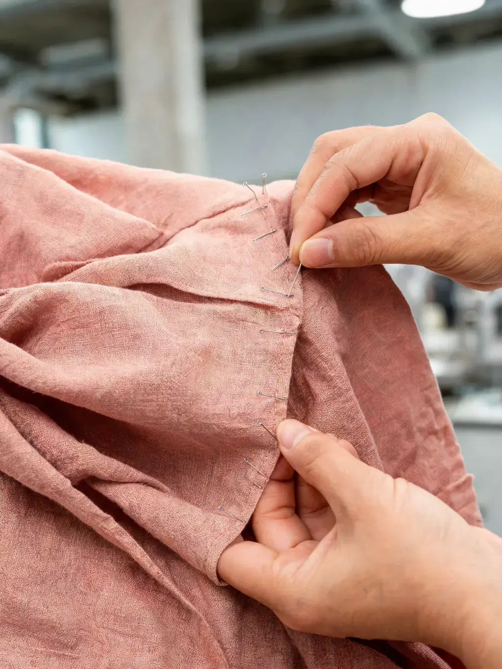 Mains épinglant tissu lin rose pour ajustement couture – épingles à tête, gros plan, atelier