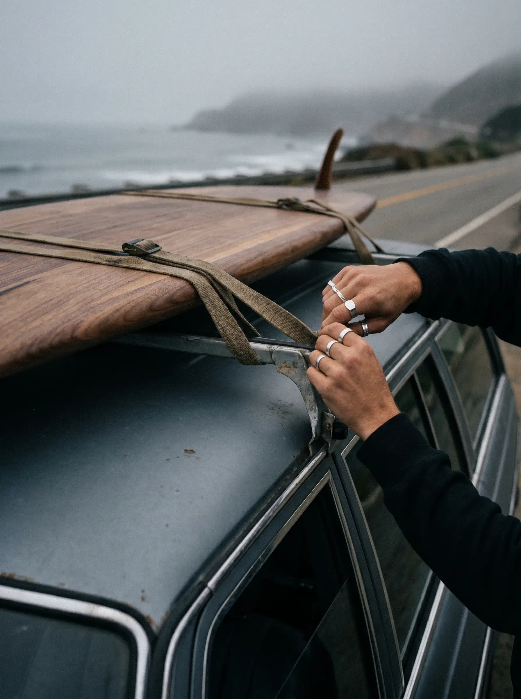 Mains fixant une planche de surf en bois sur le toit d'une voiture sur route côtière