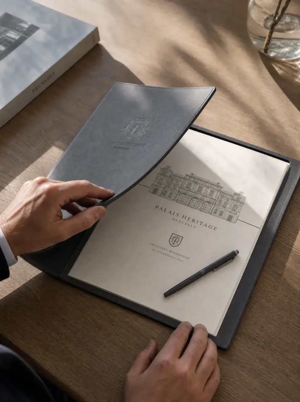 Mains ouvrant un dossier de présentation en cuir gris Palais Heritage avec dessin architectural et stylet