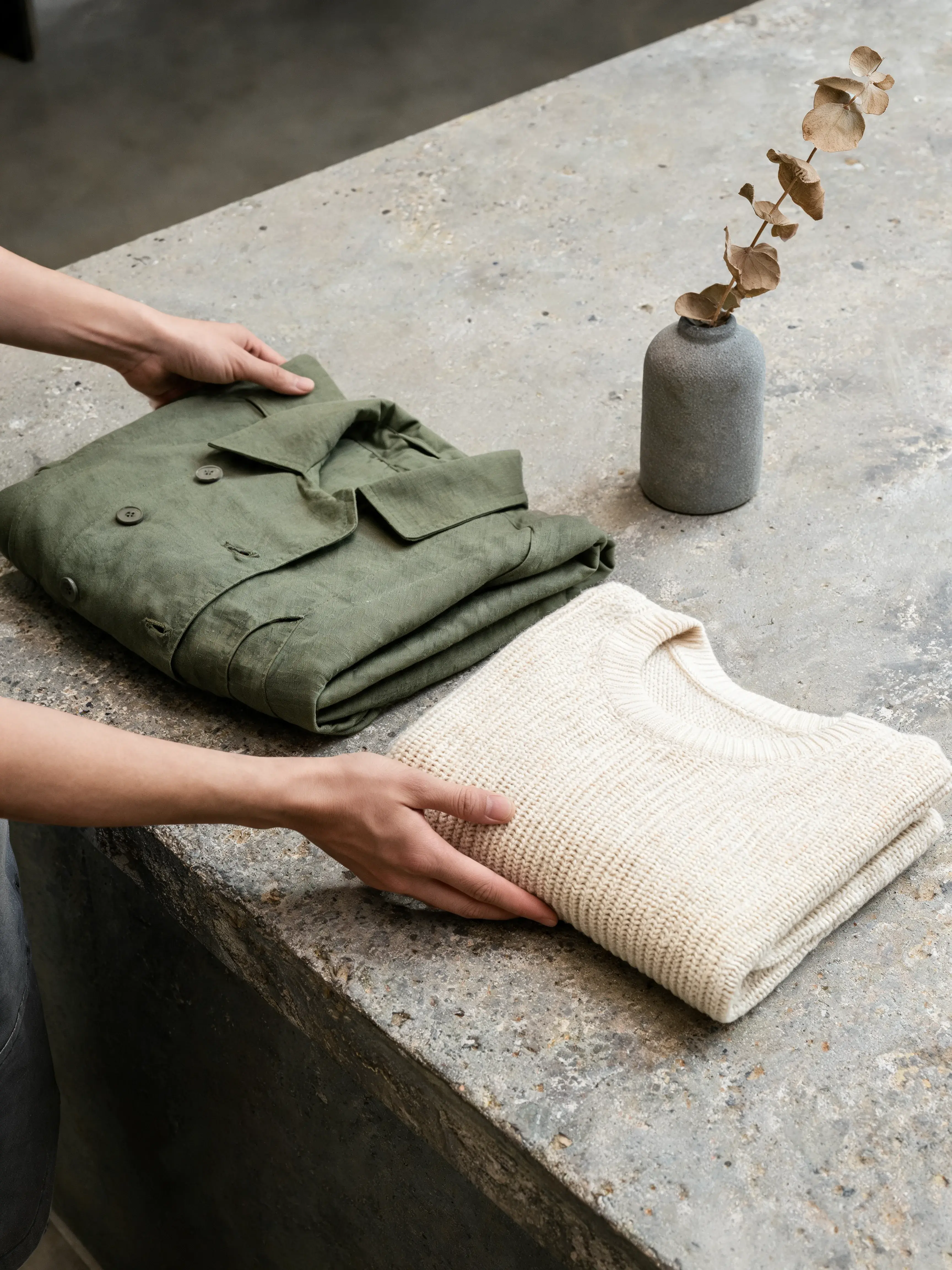 Mains pliant vêtements – chemise kaki et pull tricoté crème, comptoir granit, vase céramique
