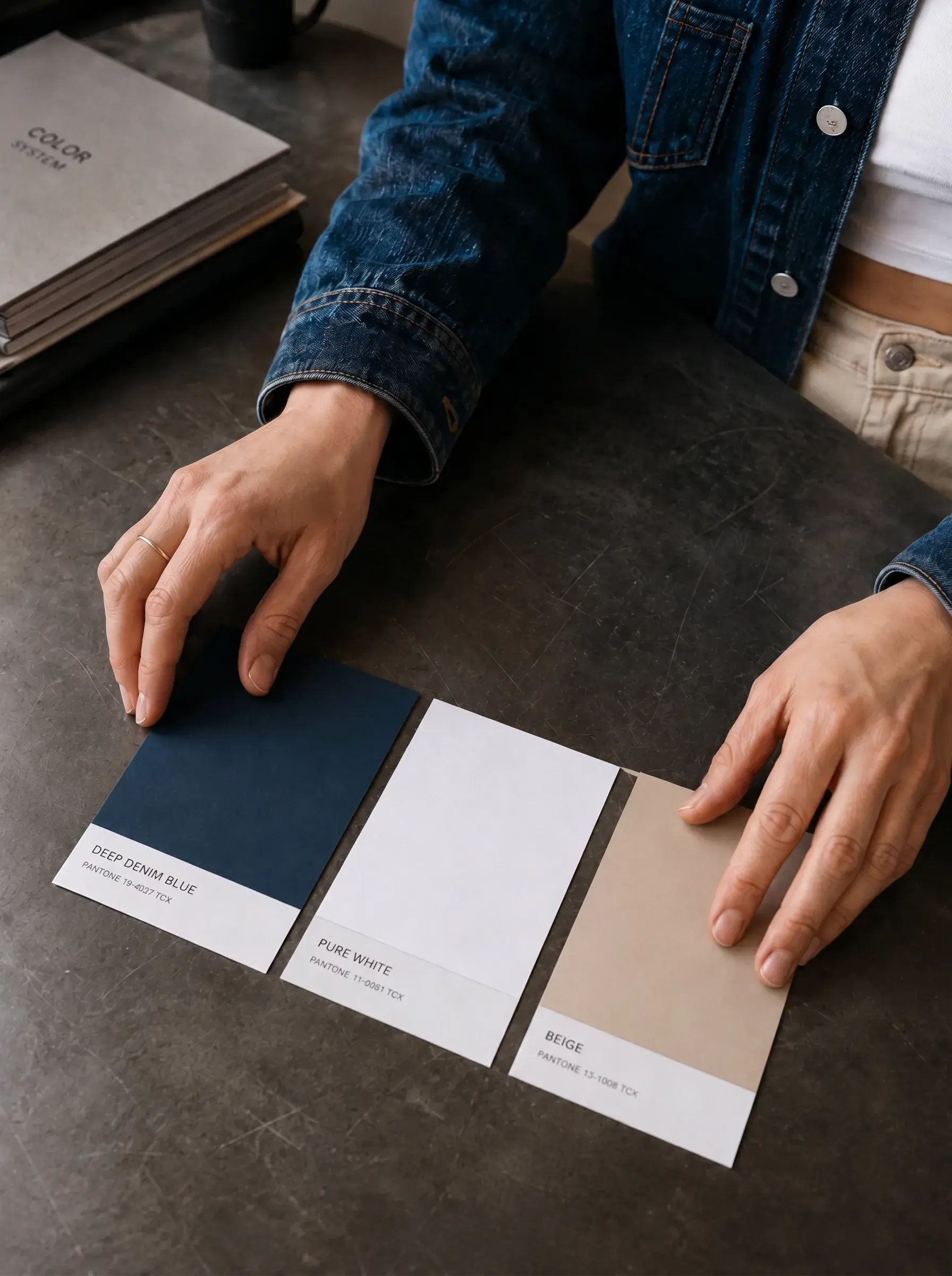 Mains posant trois cartons de couleur sur table béton – bleu marine, blanc, beige, références colorimétriques