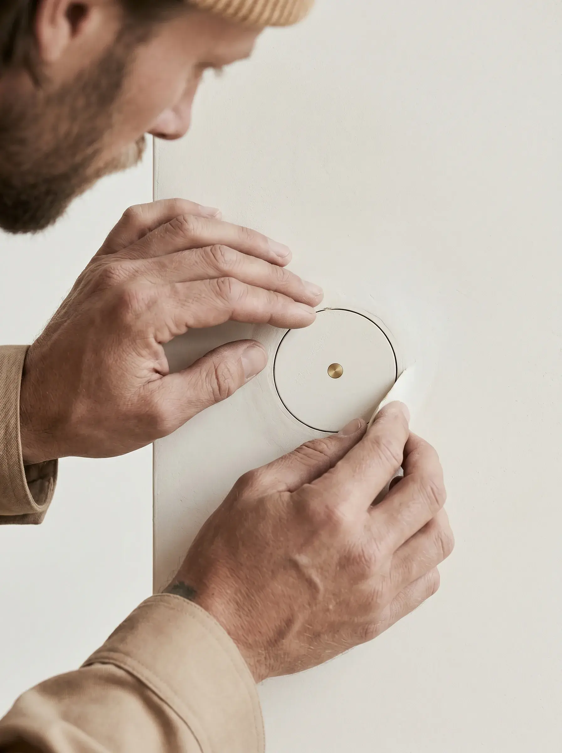 Mains posant un détecteur rond blanc à bouton laiton sur un mur clair