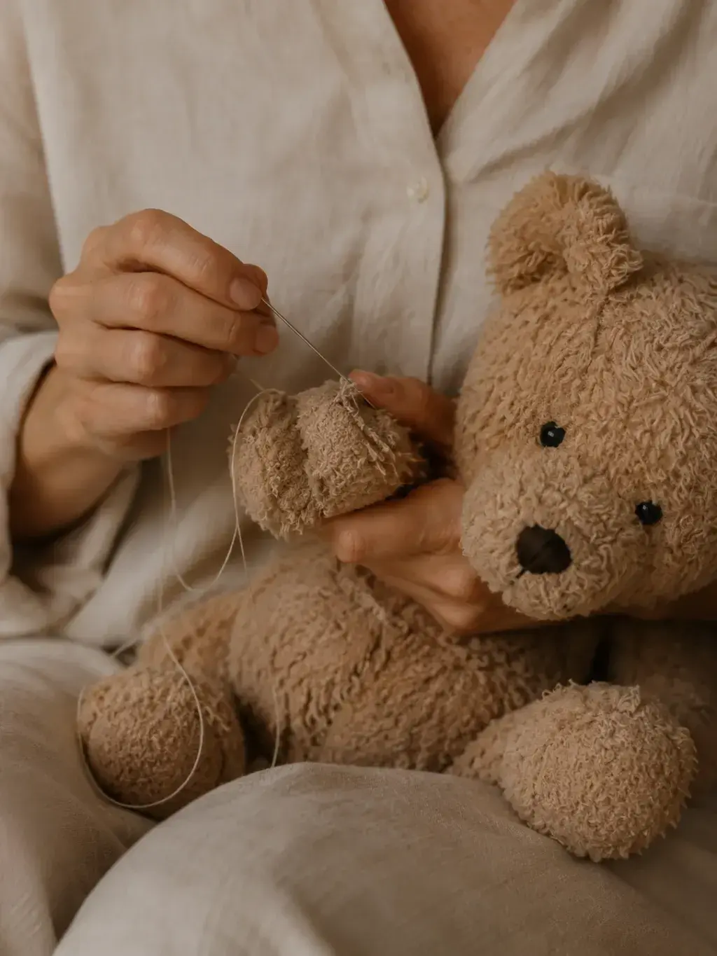 Mains recousant un nounours abîmé sur les genoux
