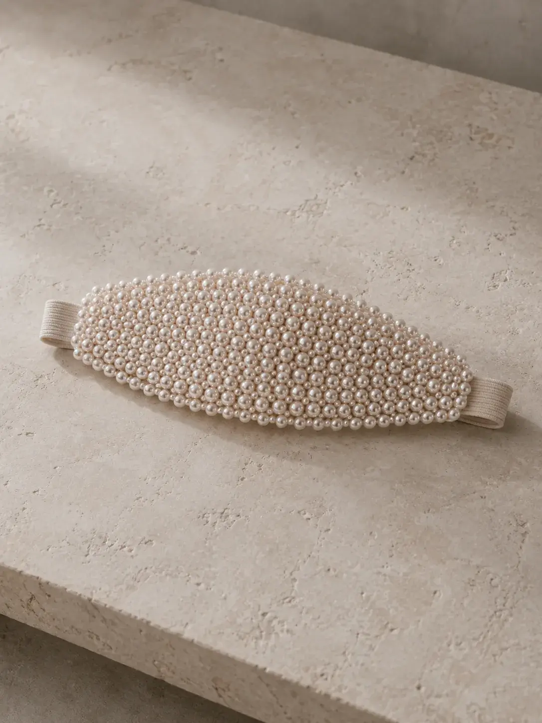 Masque de nuit ovale incrusté de perles calibrées posé sur une surface de travertin beige