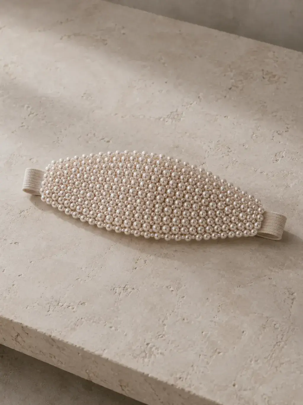 Masque de nuit ovale incrusté de perles calibrées posé sur une surface de travertin beige