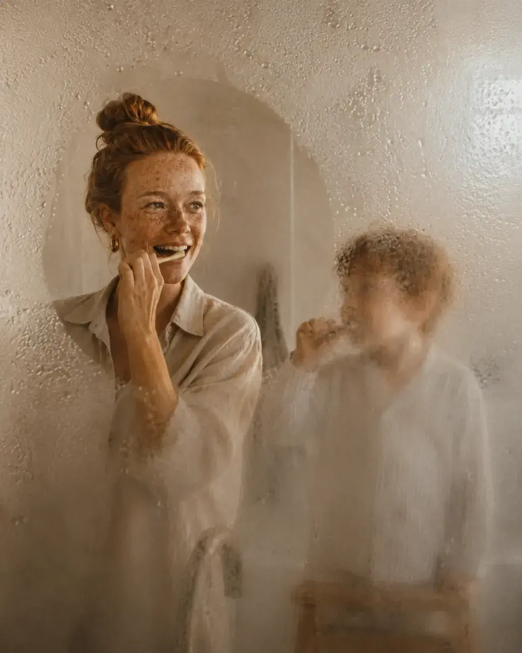 Mère et enfant roux se brossant les dents – vus à travers un miroir embué de salle de bain