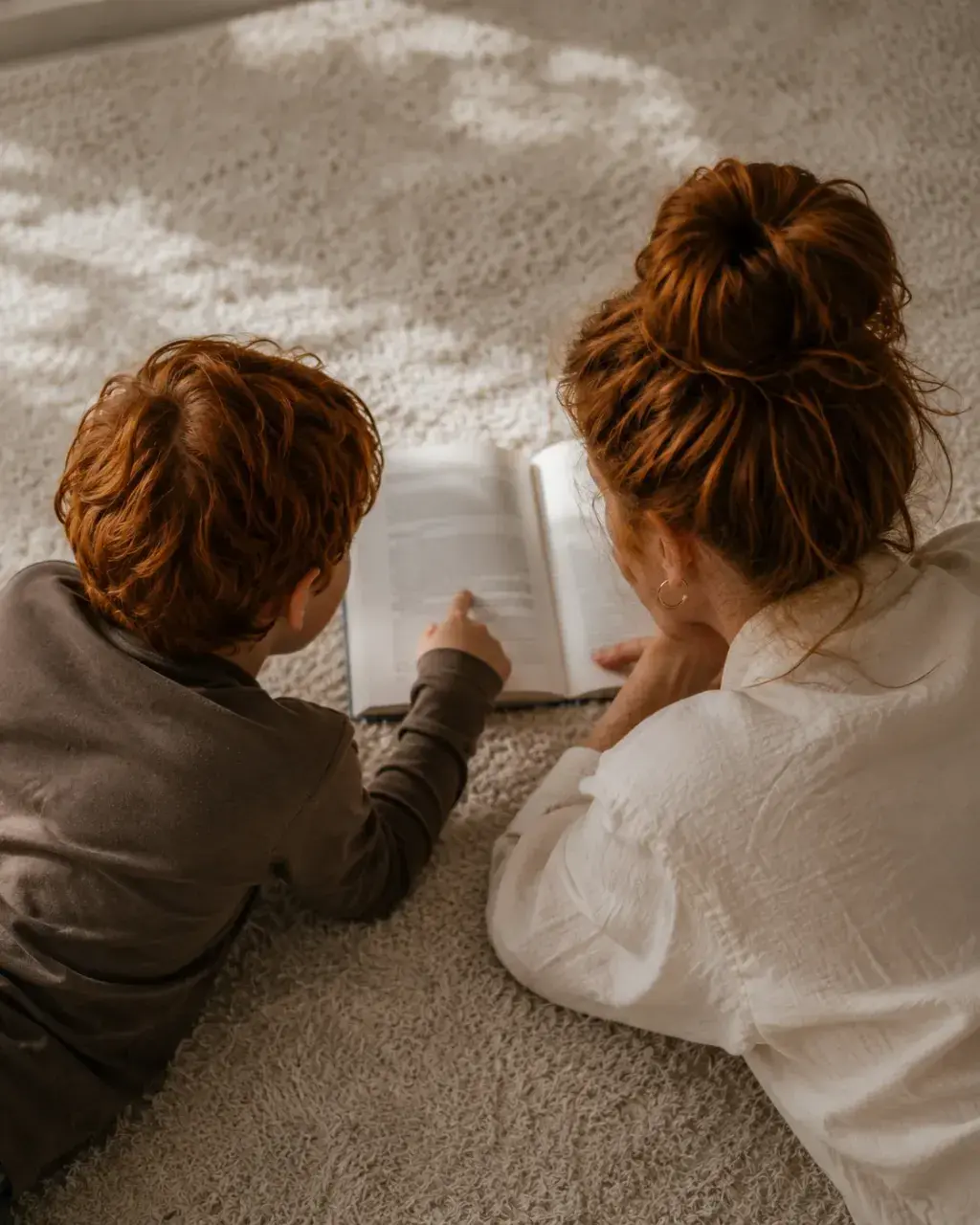Mère et fils lisant un livre ensemble allongés sur le tapis