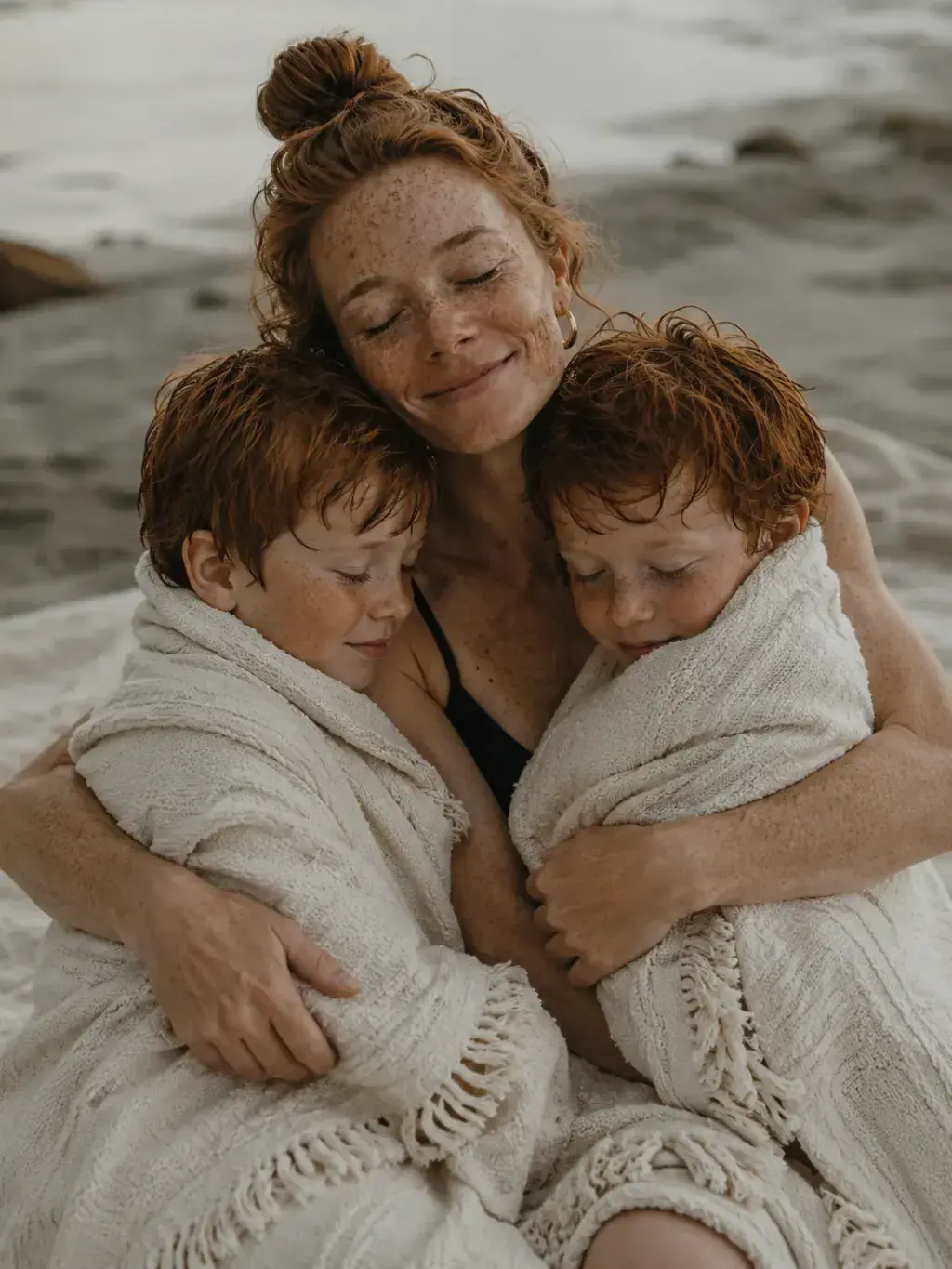 Mère serrant ses fils enroulés dans des serviettes à la plage