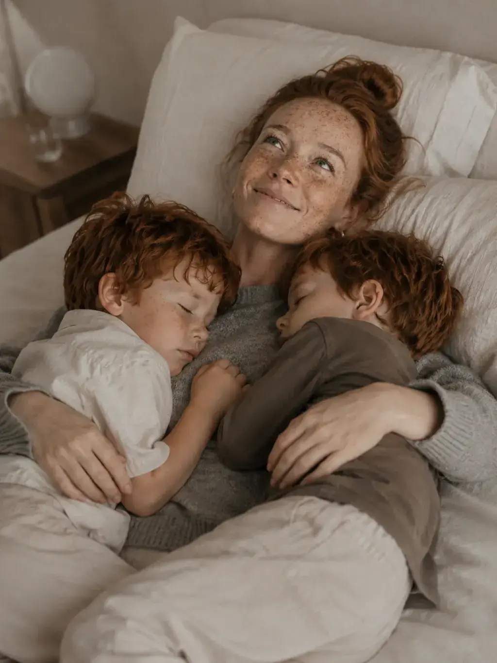 Mère souriante avec ses fils endormis dans ses bras au lit