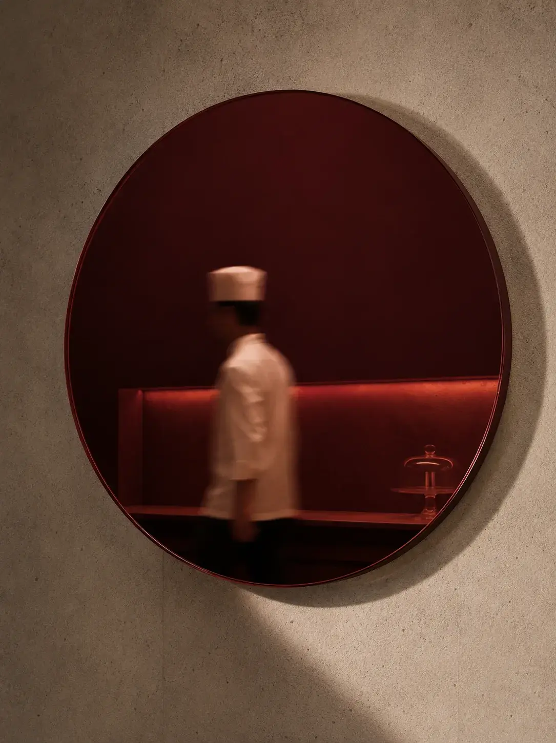 Miroir circulaire bordeaux sur mur beige – silhouette de cuisinier en toque, brasserie rouge en reflet