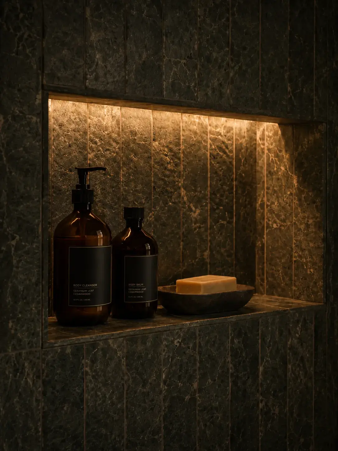 Niche de douche en marbre vert sombre avec éclairage LED doré, flacons ambre et savon en coupelle ardoise