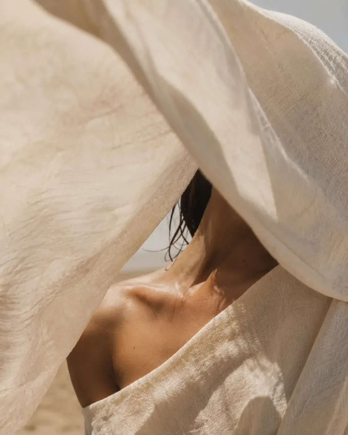 Nuque et épaule de femme partiellement voilée de tissu lin blanc – désert flou, lumière douce