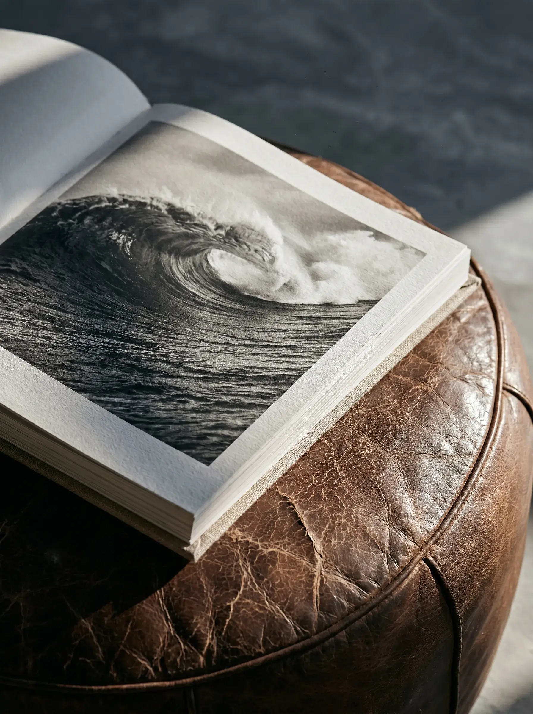 Ouvrage de photographie surf ouvert sur une vague en noir et blanc posé sur pouf cuir