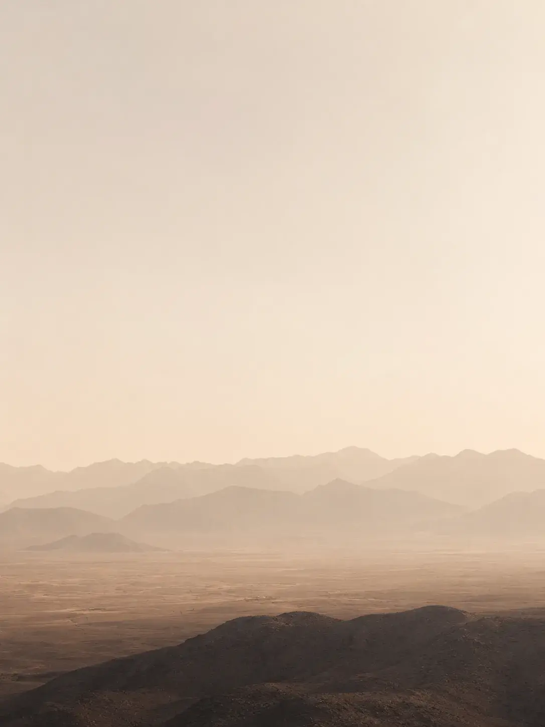 Paysage désertique brumeux en couches – silhouettes de montagnes rosées, brume dorée, ciel pâle