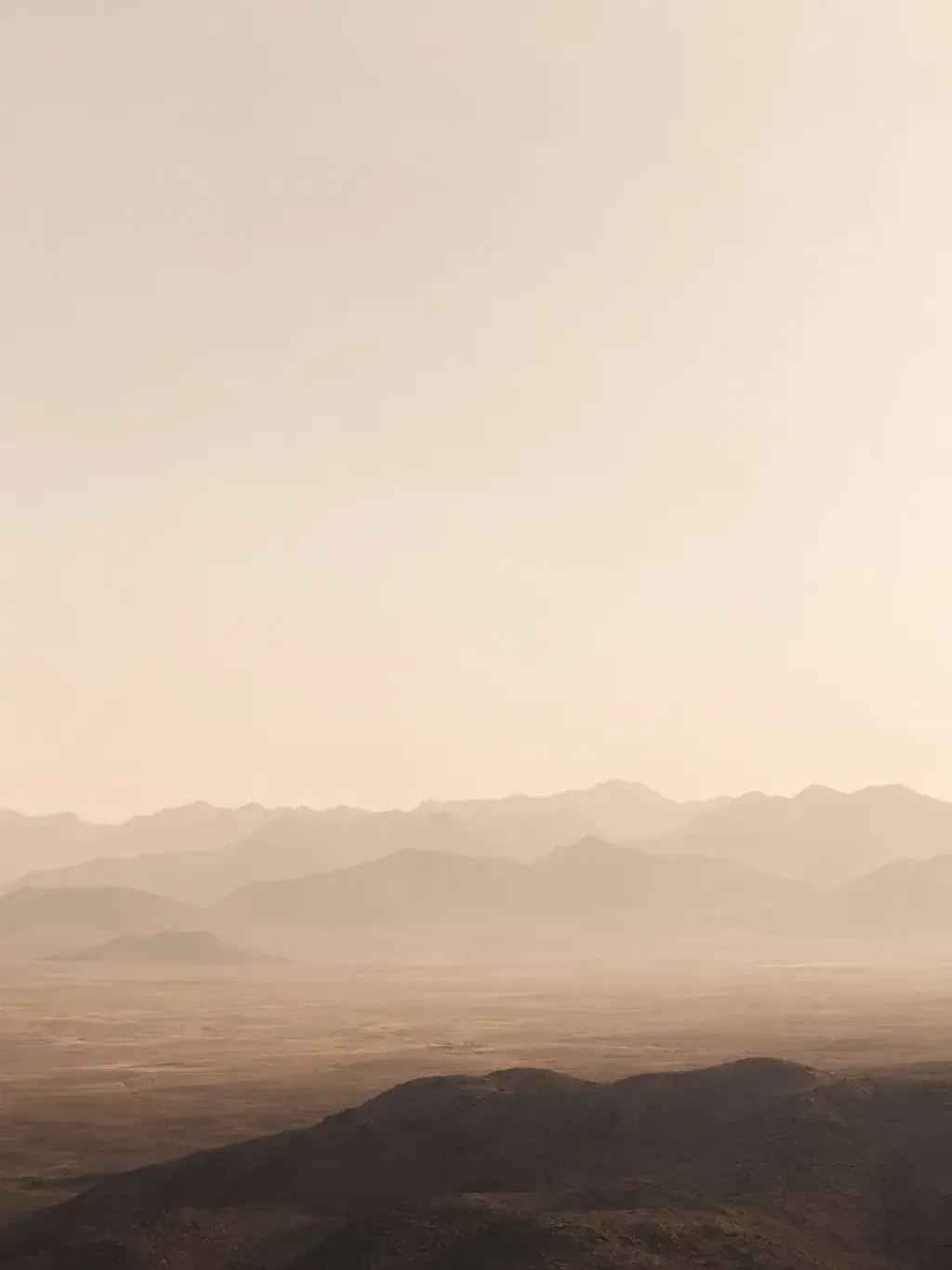 Paysage désertique brumeux en couches – silhouettes de montagnes rosées, brume dorée, ciel pâle