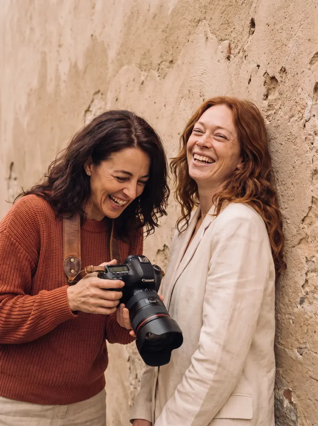 Photographe brune et modèle rousse riant ensemble contre un mur en pierre en extérieur
