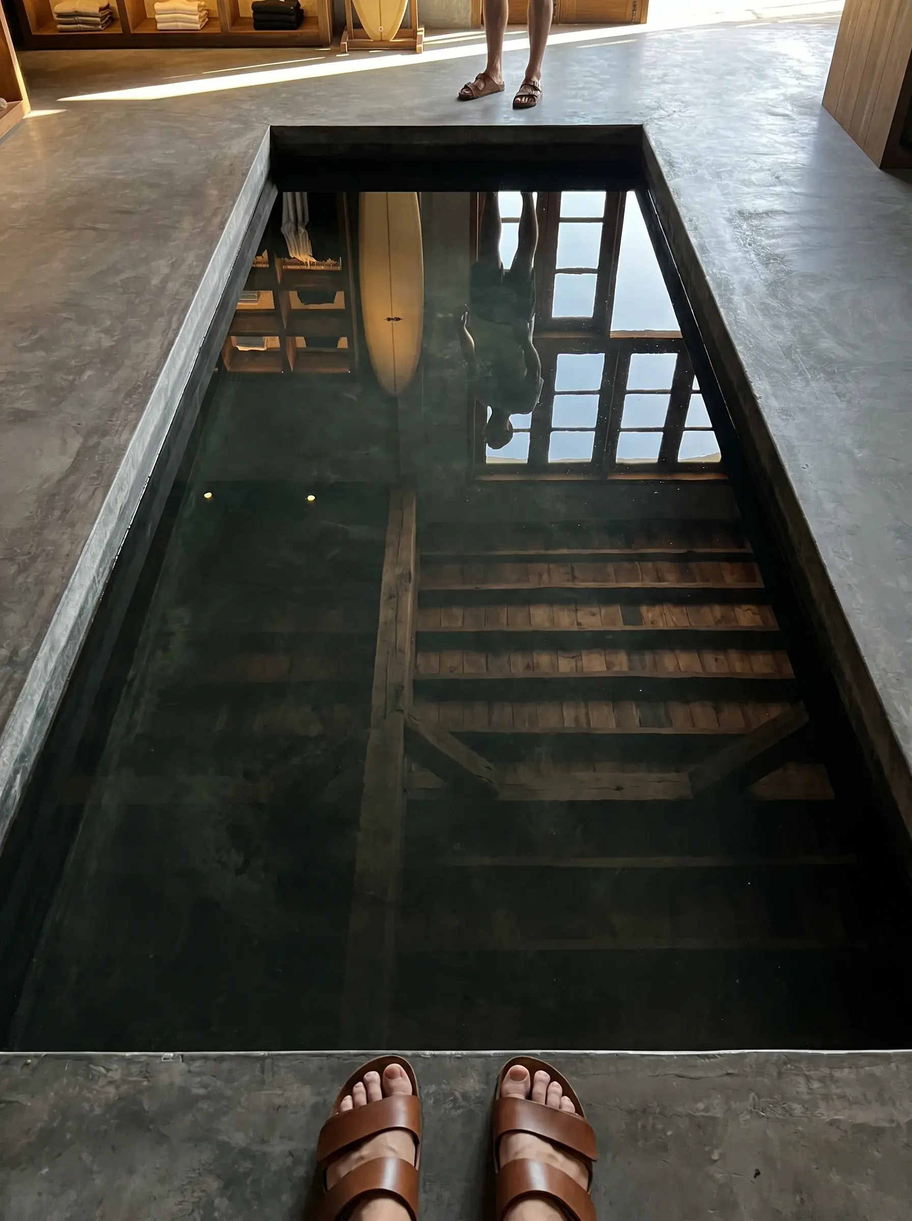 Pieds en sandales en cuir au bord d'un bassin réfléchissant sombre dans une boutique