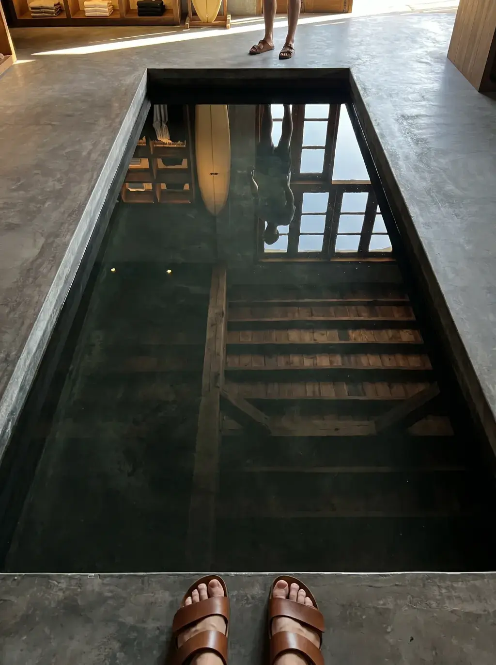 Pieds en sandales en cuir au bord d'un bassin réfléchissant sombre dans une boutique