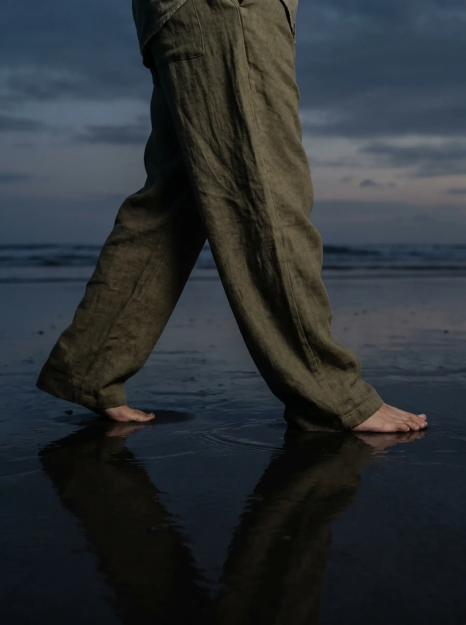 Pieds nus et bas de pantalon kaki en lin sur sable volcanique noir mouillé