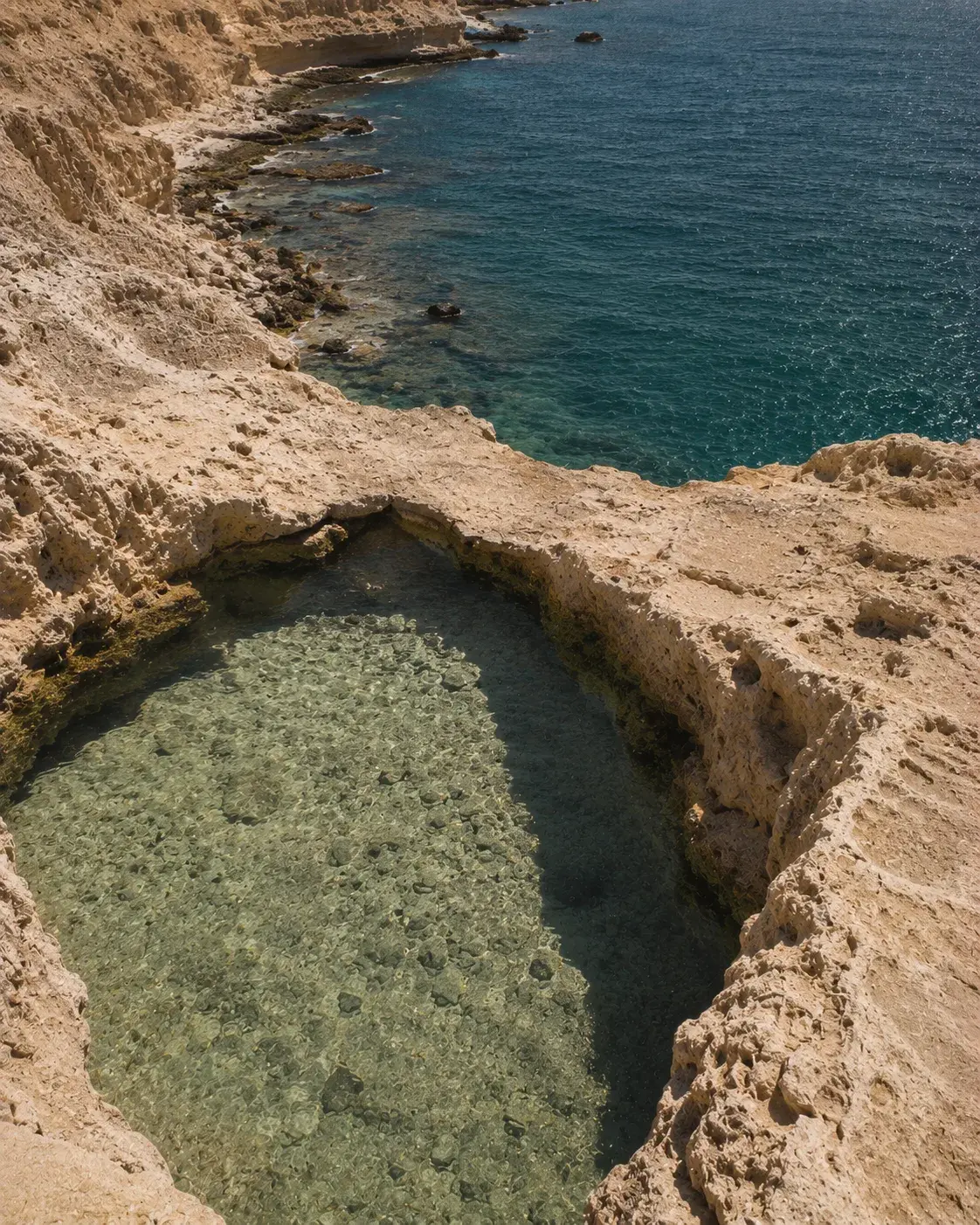 Piscine naturelle creusée dans rocher calcaire – eau turquoise et mer bleue en contrebas