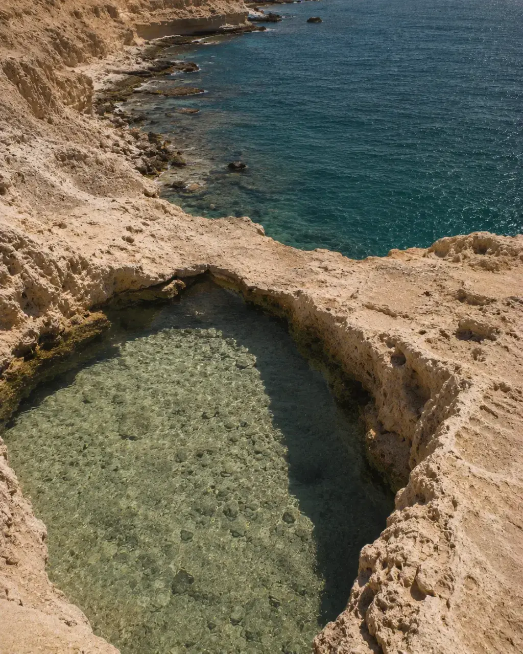 Piscine naturelle creusée dans rocher calcaire – eau turquoise et mer bleue en contrebas