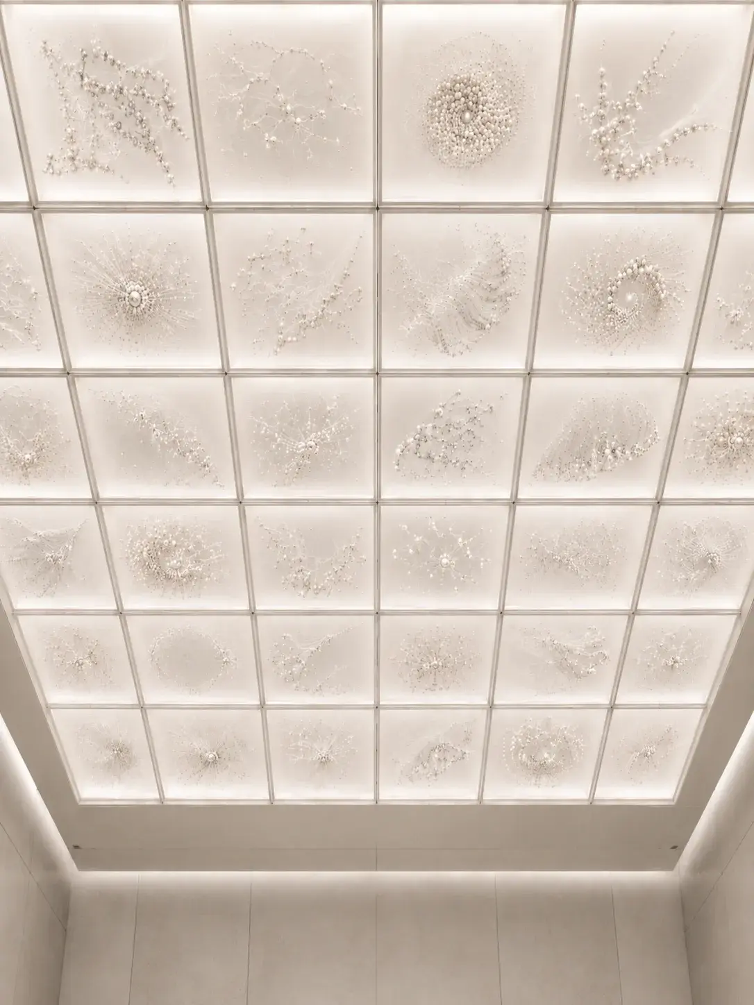 Plafond à caissons blancs avec installations artistiques en perles et textiles dans chaque panneau, vue en contre-plongée