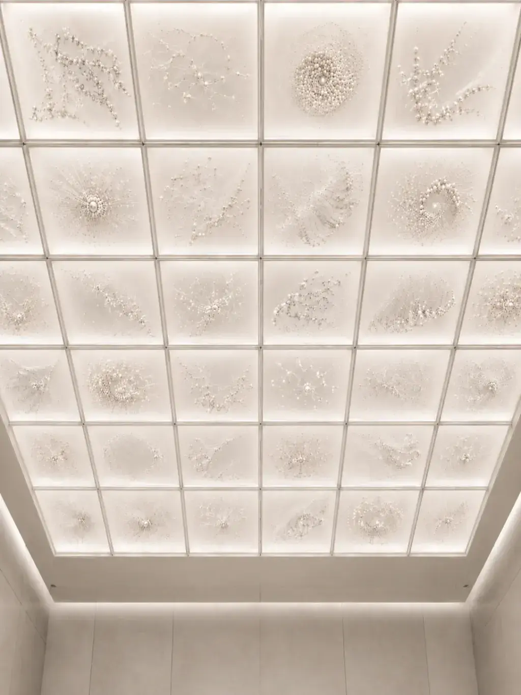 Plafond à caissons blancs avec installations artistiques en perles et textiles dans chaque panneau, vue en contre-plongée