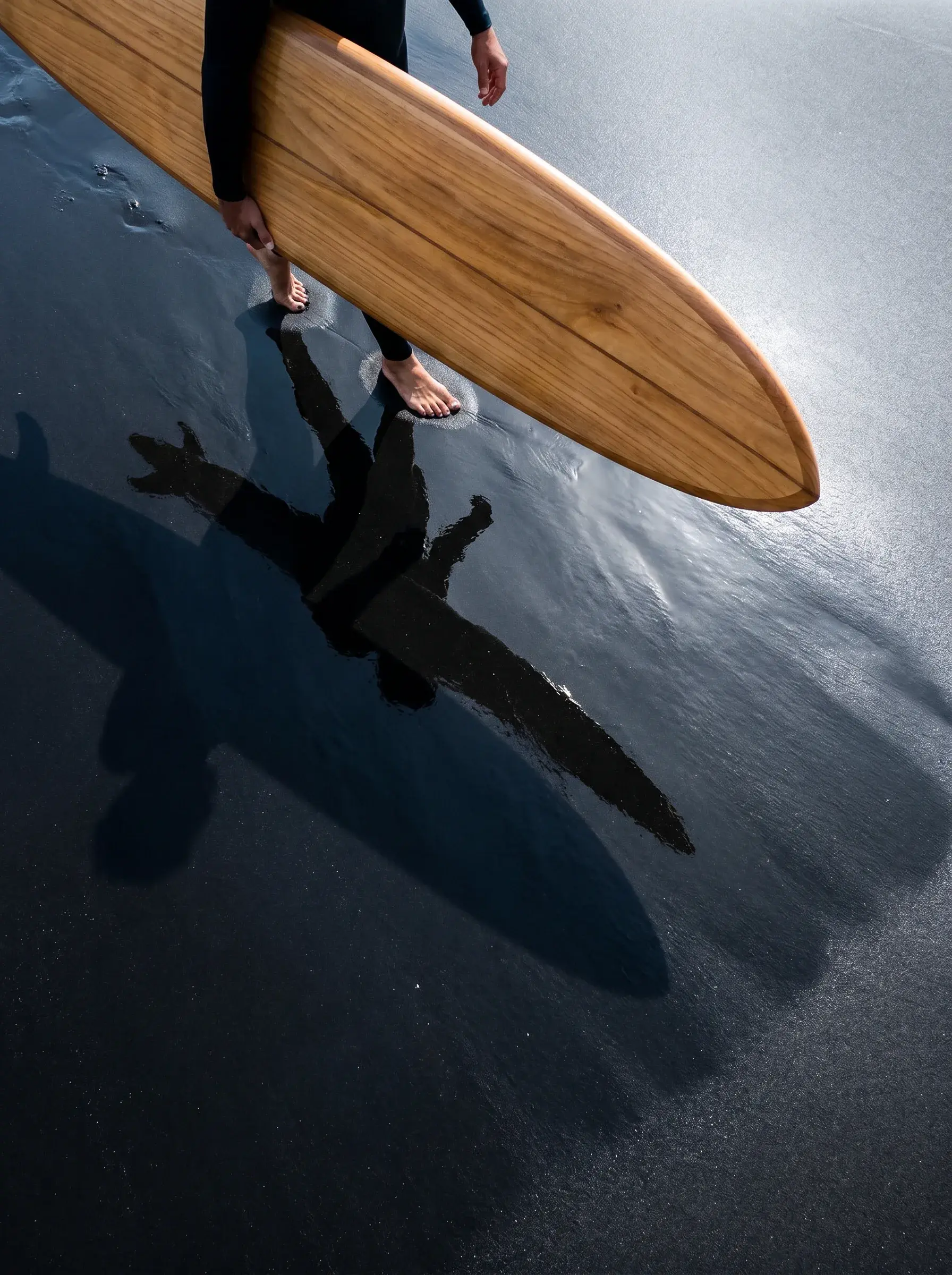 Planche de surf en bois portée au-dessus du sable noir mouillé avec ombre projetée