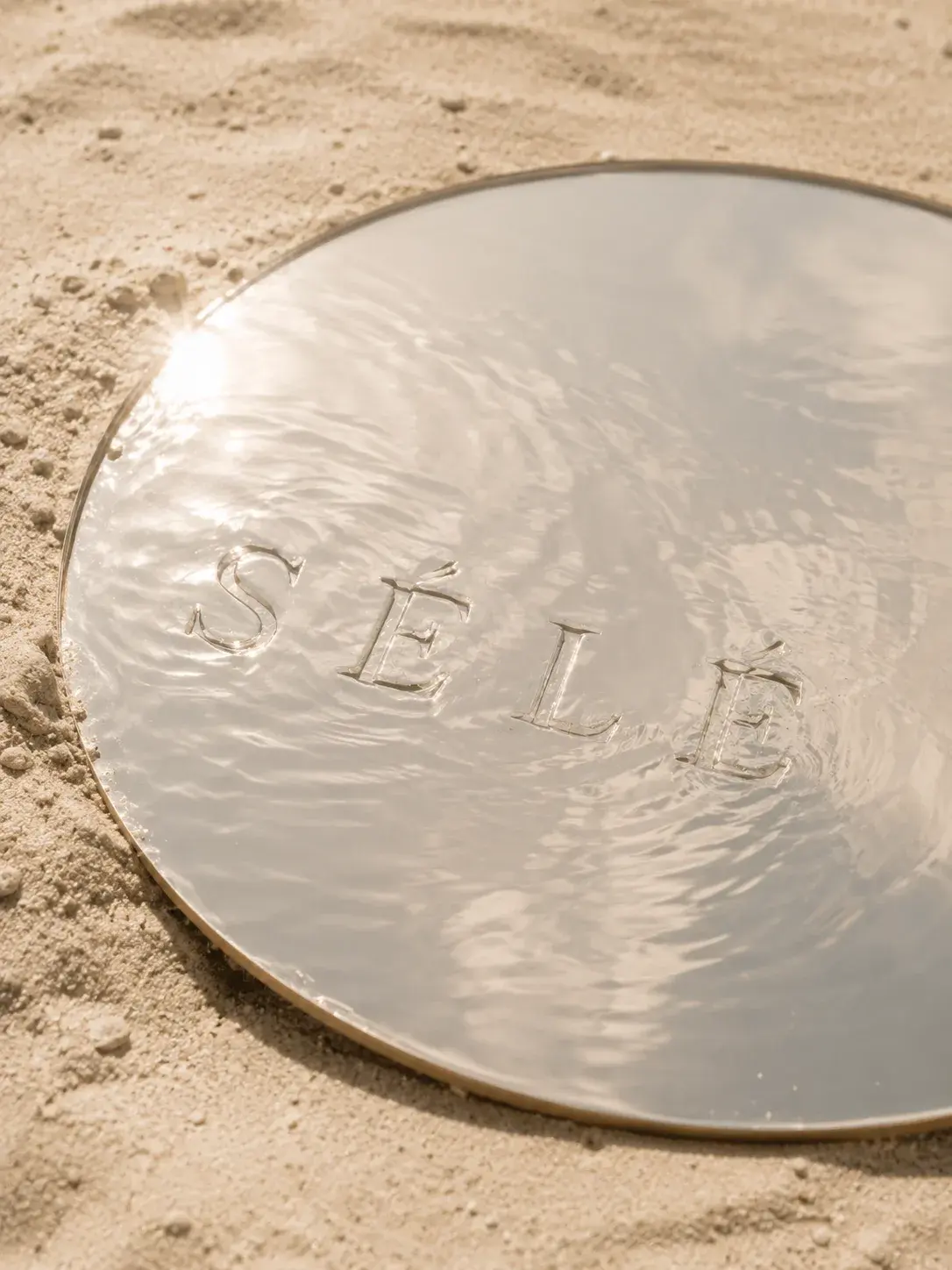 Plateau miroir rond sur sable avec reflets de soleil et eau – inscription gravée, lumière estivale