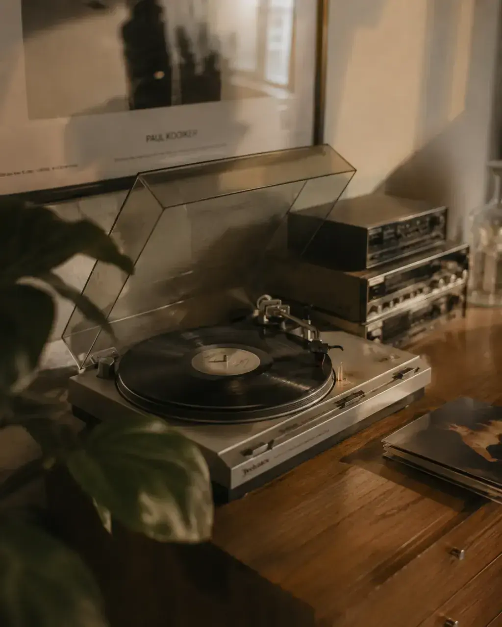 Platine vinyle sur meuble en bois – lumière chaude dorée, plante et ampli en fond