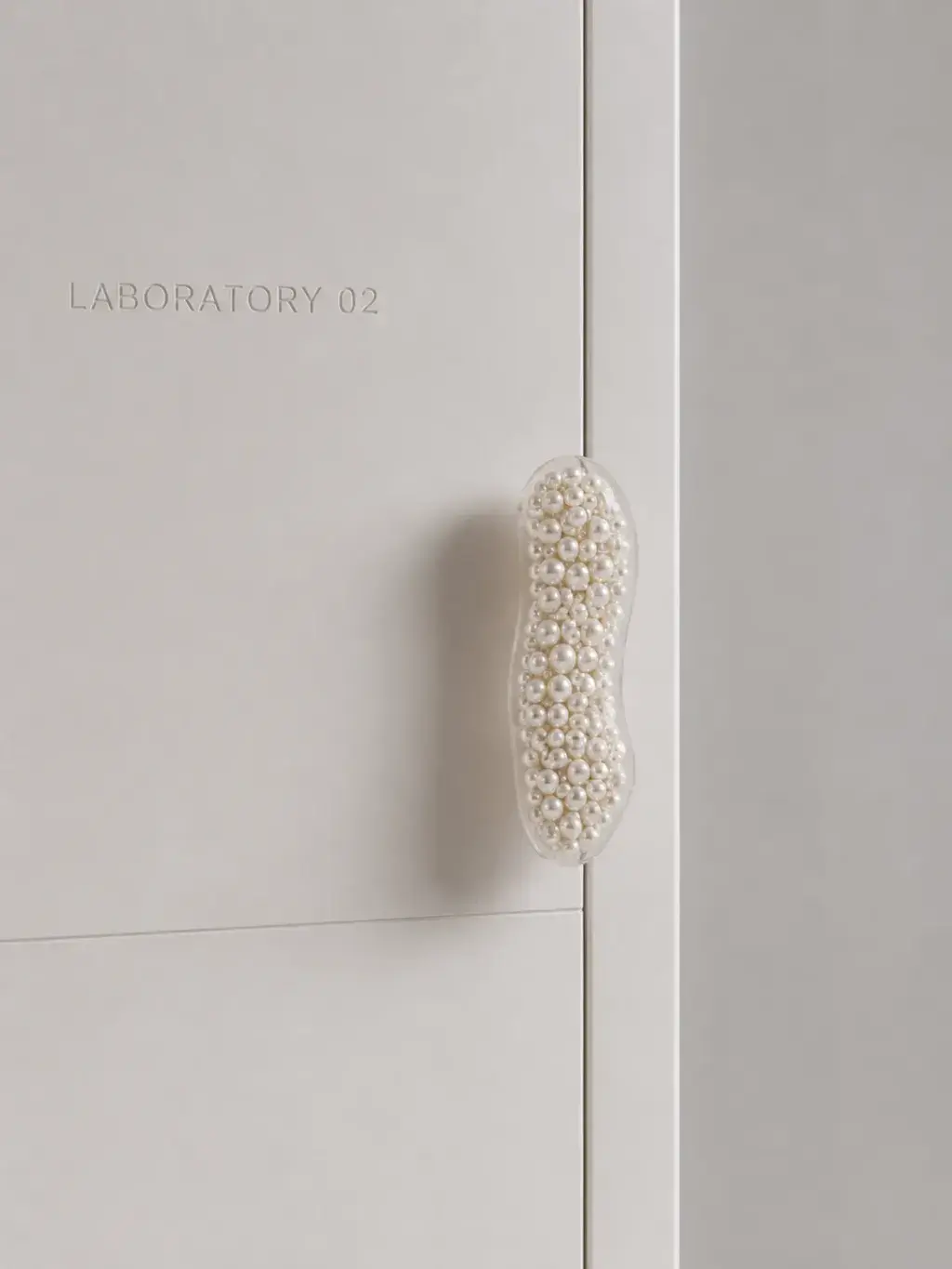 Poignée de porte recouverte de perles calibrées sur porte blanche marquée LABORATORY 02, détail nacré