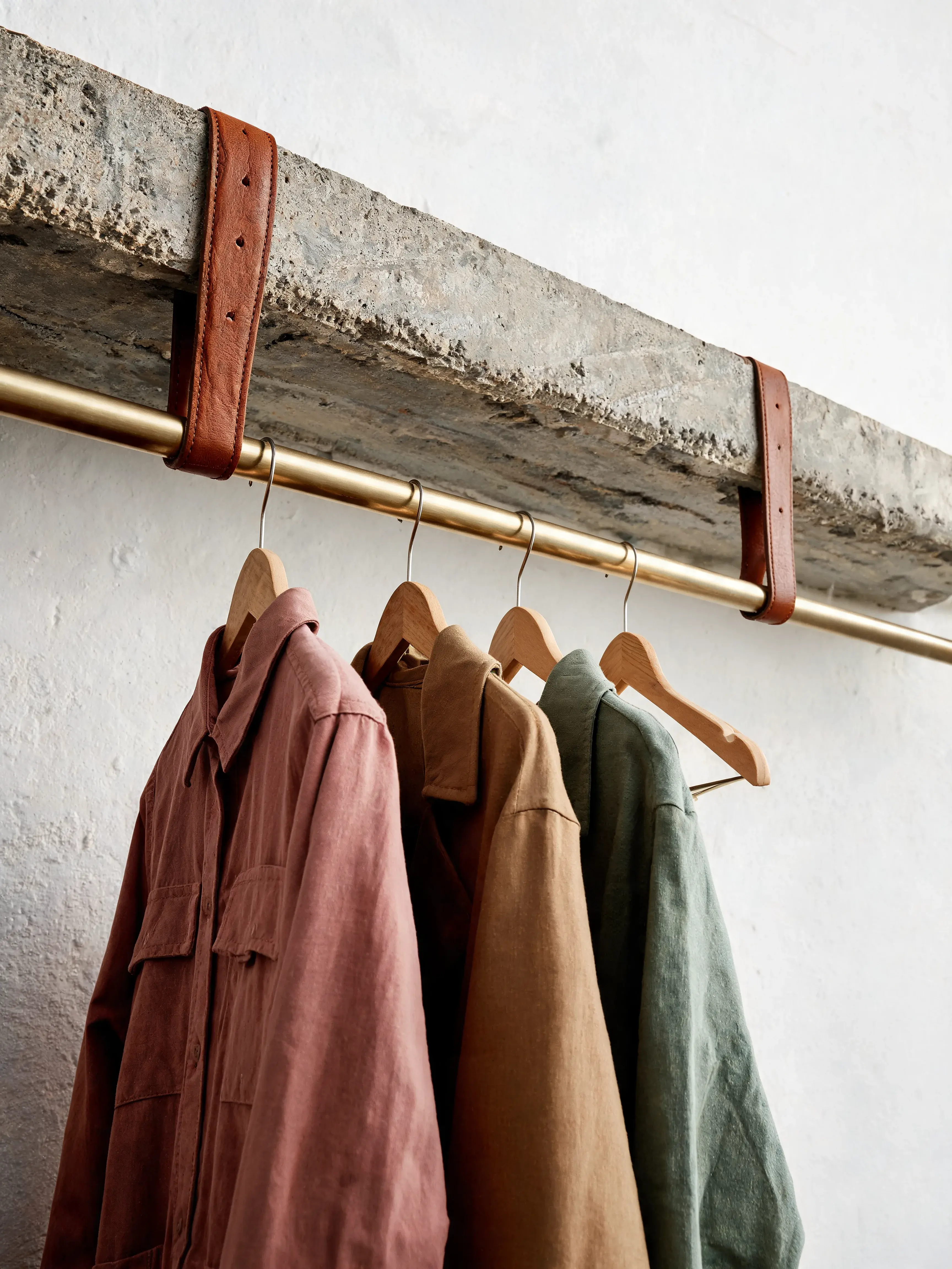 Portant laiton sangles cuir – vestes lin colorées, cintres bois, mur béton