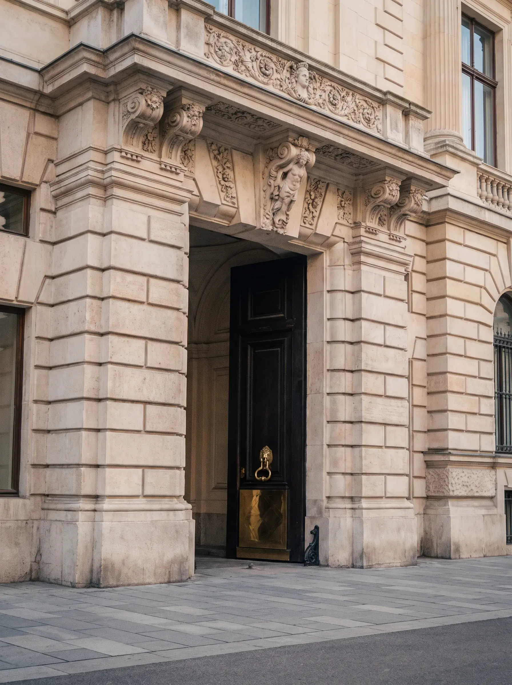 Porte cochère monumentale avec fronton sculpté de cariatides et heurtoir en laiton sur façade en pierre