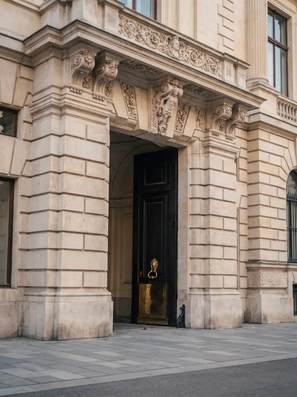 Porte cochère monumentale avec fronton sculpté de cariatides et heurtoir en laiton sur façade en pierre