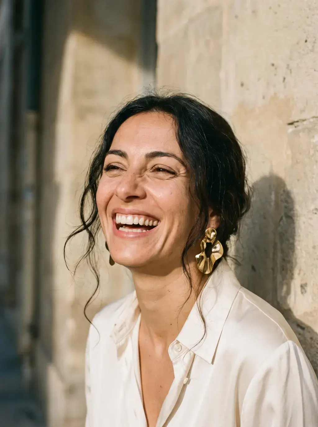 Portrait de femme brune riant aux éclats contre un mur en pierre