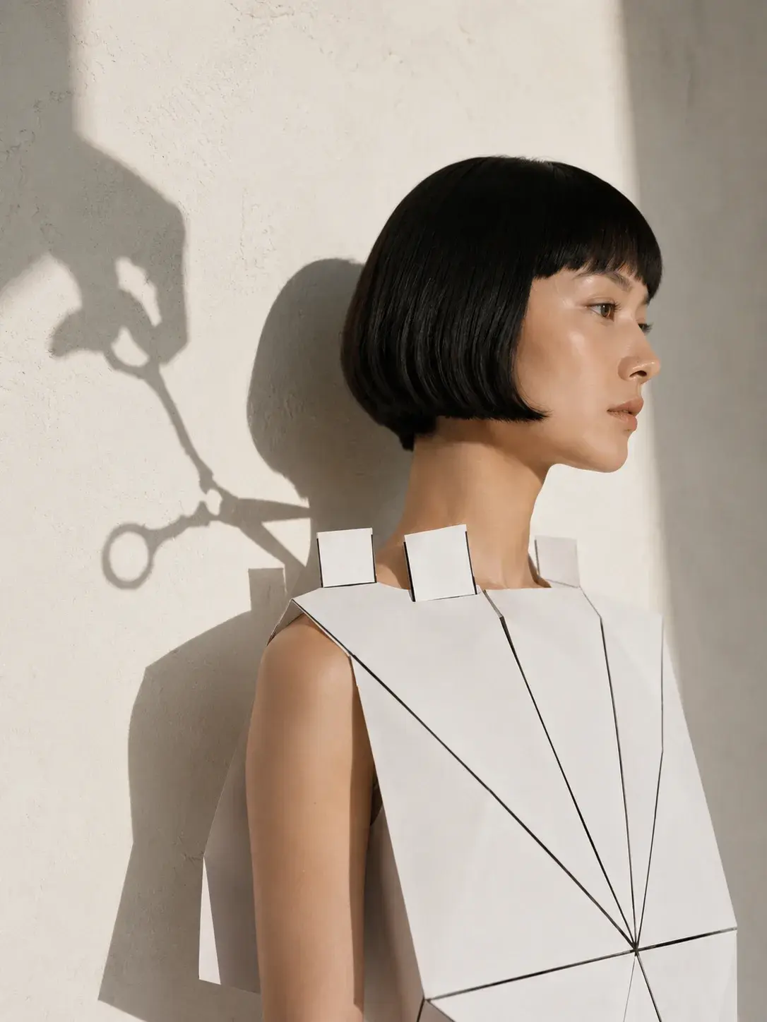 Portrait de profil femme en top origami avec ombre de ciseaux – mur beige et lumière rasante
