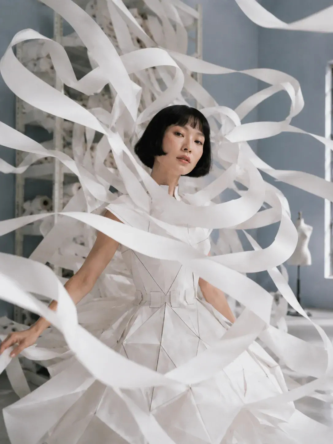 Portrait femme en robe origami dans tourbillon de rubans blancs – atelier bleu