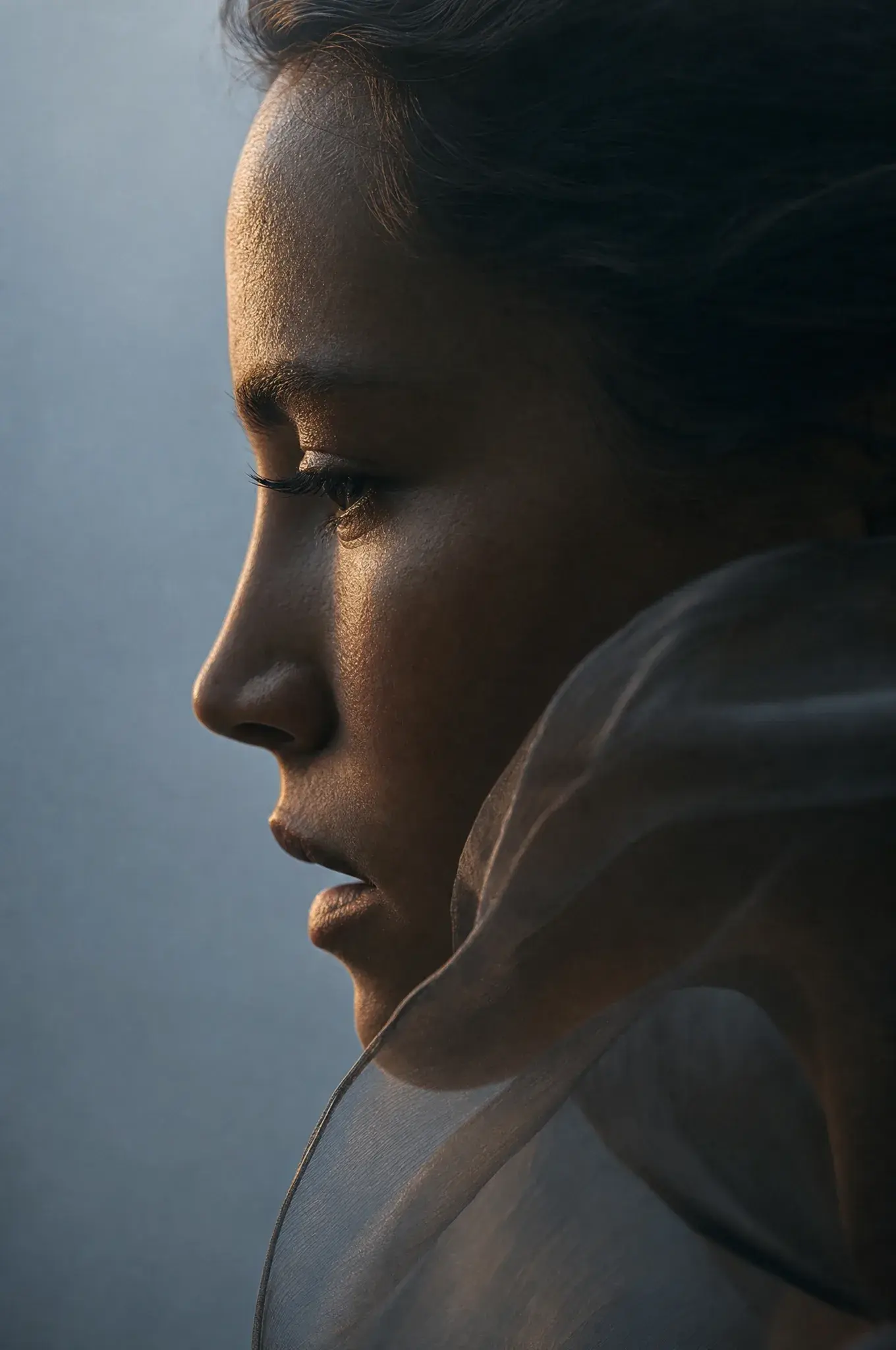Portrait gros plan profil femme – voile gaze autour du cou, lumière chaude sur visage, fond bleu