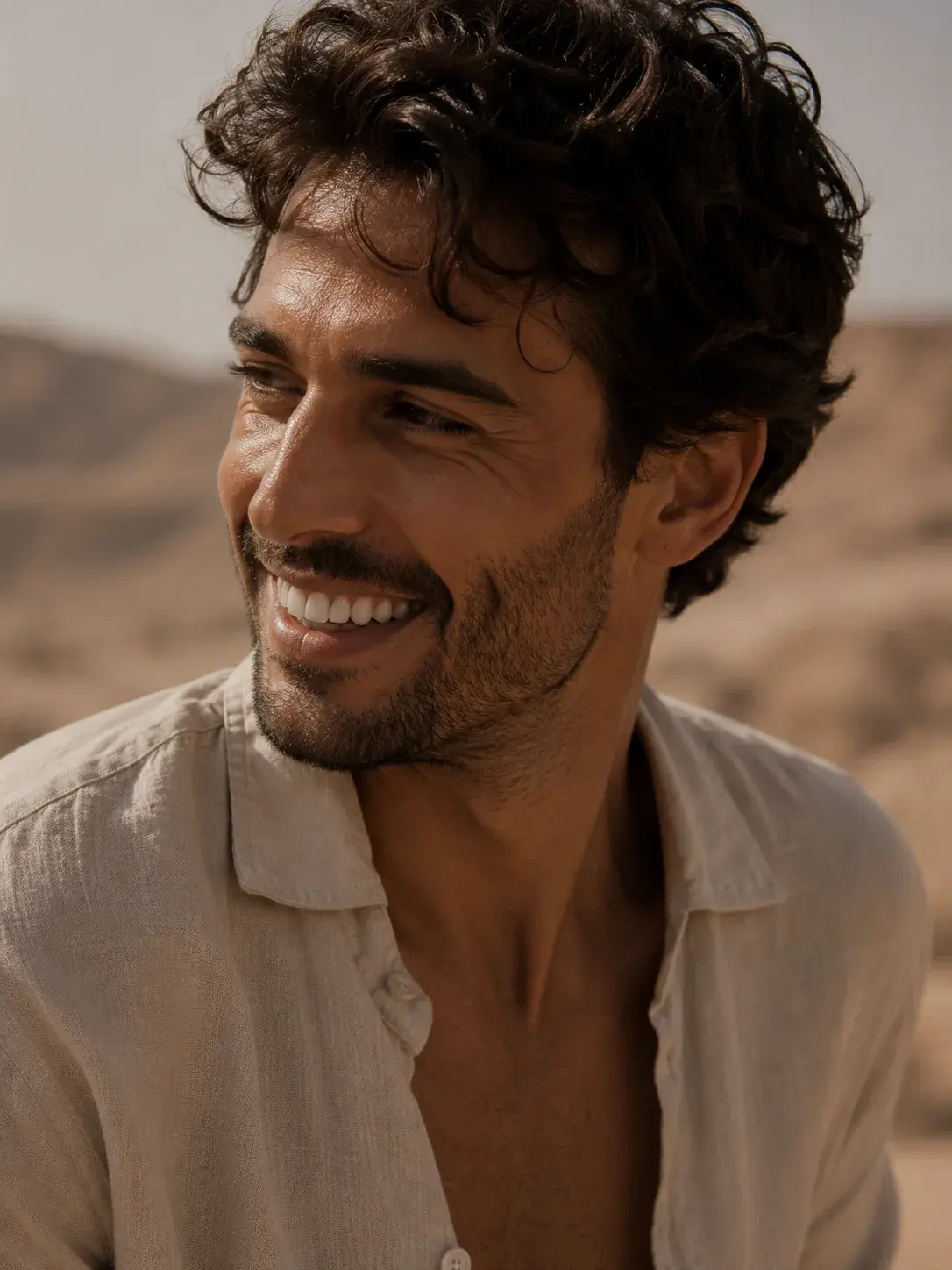 Portrait homme souriant en chemise lin – cheveux bouclés, barbe, paysage désertique, lumière dorée